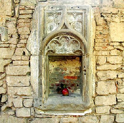 Mittelalterliche steinerne Wandnische mit gotischem Maßwerk, darin ein Apfel.