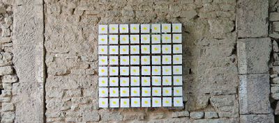 64 quadratische, mit einem gelben Punkt bestempelte Papierkärtchen an altem Gemäuer